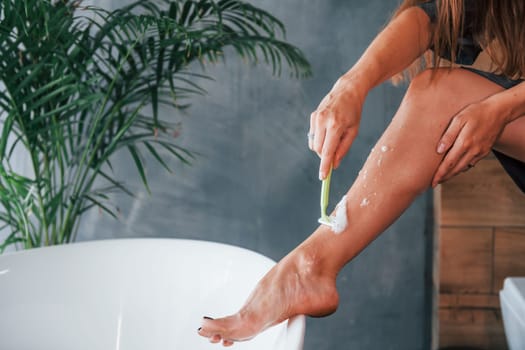 Beautiful young woman have free time at home in the bath. Shaves legs.