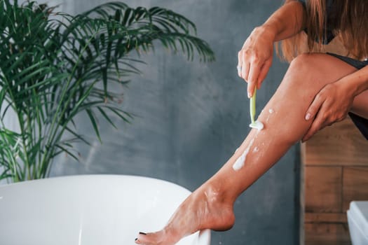 Beautiful young woman have free time at home in the bath. Shaves legs.