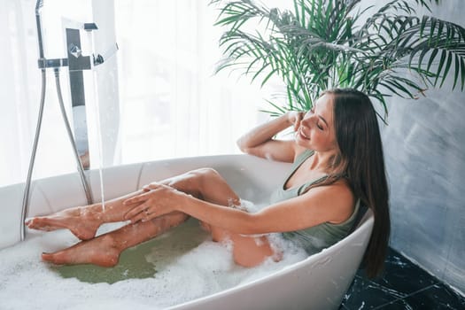 Uses phone. Beautiful young woman have free time at home in the bath.