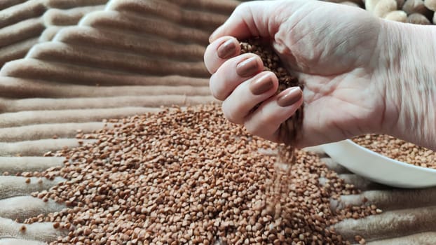 Brown buckwheat groats and hand of woman in it. Food for background and texture. Product and food that can be stored for long time. Partial focus