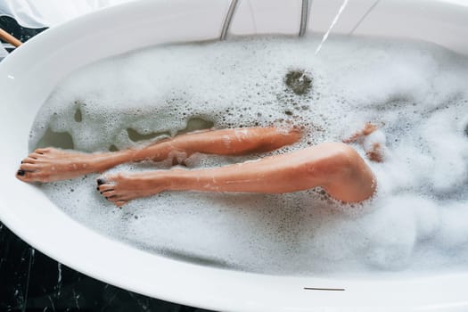 Particle view of legs. Beautiful young woman have free time at home in the bath.