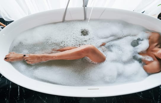 Particle view of legs. Beautiful young woman have free time at home in the bath.