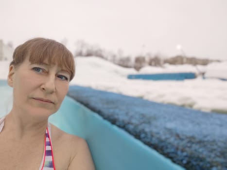 Adult mature woman takes selfie in a pool with warm hot termal mineral water in winter and white snow around. Wellness center and the concept of health care. Travel, recreation, medicine and rest