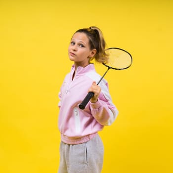 Full length studio photo of ten year old girl holding a badminton racket and isolated on yellow.