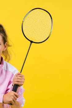 Full length studio photo of ten year old girl holding a badminton racket and isolated on yellow.