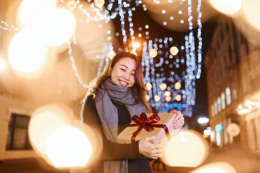 With gift box. Cute and happy asian young woman outdoors in the city celebrates New year.