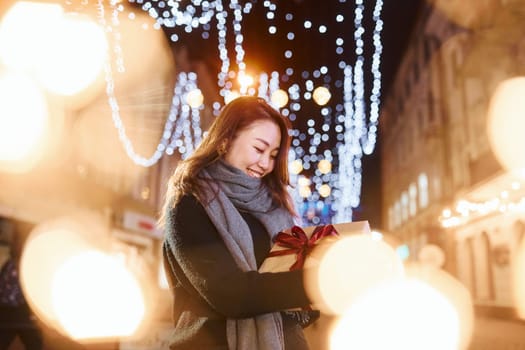 With gift box. Cute and happy asian young woman outdoors in the city celebrates New year.