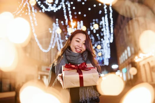 With gift box. Cute and happy asian young woman outdoors in the city celebrates New year.