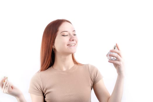 Happy young caucasian woman using perfume, holding glass bottle isolated on white background