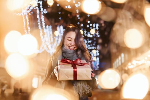With gift box. Cute and happy asian young woman outdoors in the city celebrates New year.