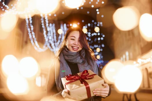 With gift box. Cute and happy asian young woman outdoors in the city celebrates New year.