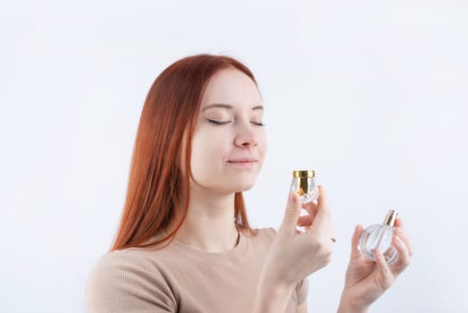 Happy young caucasian woman smelling perfume, holding glass bottle isolated on white background