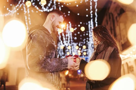 Holds gift box. Happy multiracial couple together outdoors in the city celebrating New year.