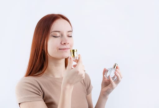 Happy young caucasian woman smelling perfume, holding glass bottle isolated on white background