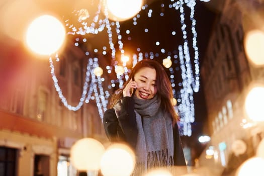 Talks by phone. Cute and happy asian young woman outdoors in the city celebrates New year.