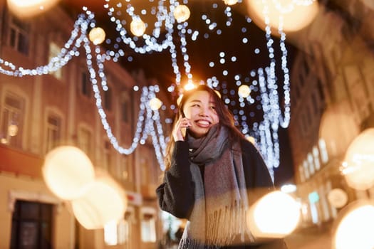 Talks by phone. Cute and happy asian young woman outdoors in the city celebrates New year.