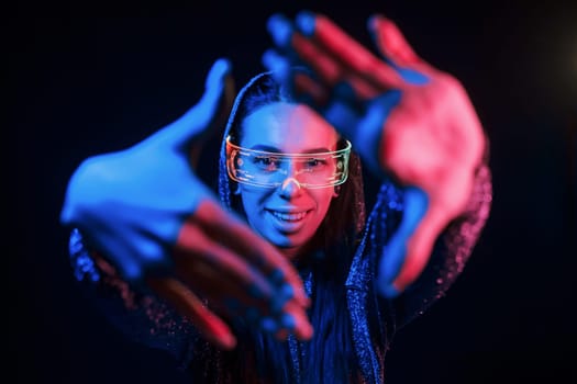 Does gestures by hands. Portrait of young girl that is in eyeglasses in blue neon lighting.