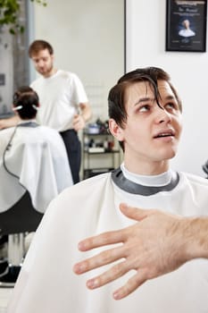 Barber talking to young client man before haircut at barbershop. client tells what haircut he wants