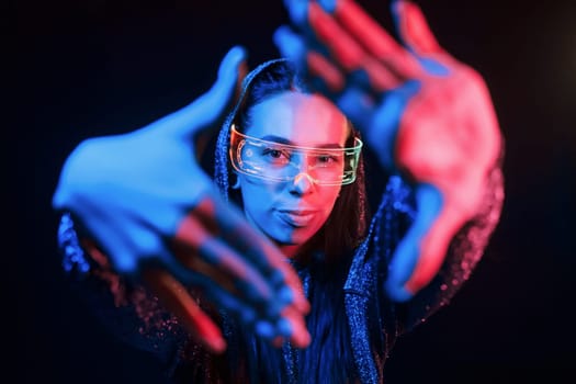 Does gestures by hands. Portrait of young girl that is in eyeglasses in blue neon lighting.