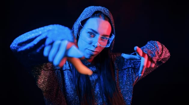 Does gestures by hands. Portrait of young girl that is in eyeglasses in blue neon lighting.