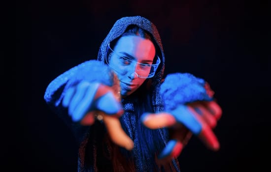 Does gestures by hands. Portrait of young girl that is in eyeglasses in blue neon lighting.