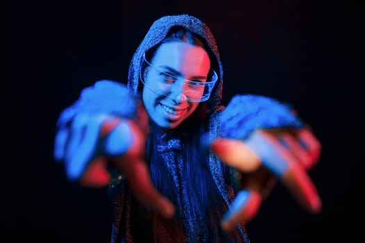 Does gestures by hands. Portrait of young girl that is in eyeglasses in blue neon lighting.