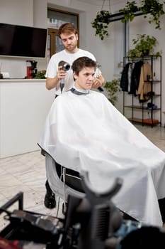 Professional hairdresser during work with man client with hair dryer in barber shop. Haircut in the barbershop.