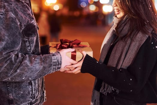 Holds gift box. Happy multiracial couple together outdoors in the city celebrating New year.