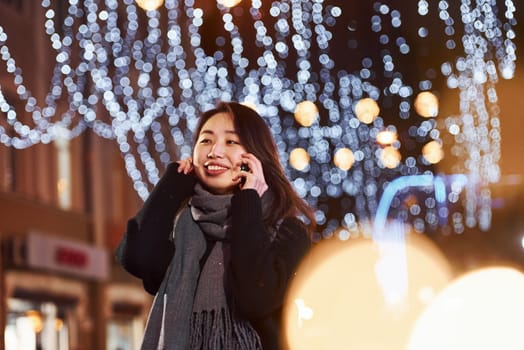 Talks by phone. Cute and happy asian young woman outdoors in the city celebrates New year.