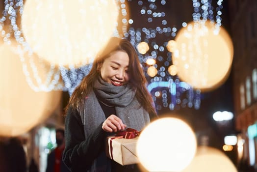 With gift box. Cute and happy asian young woman outdoors in the city celebrates New year.
