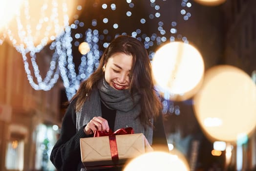 With gift box. Cute and happy asian young woman outdoors in the city celebrates New year.