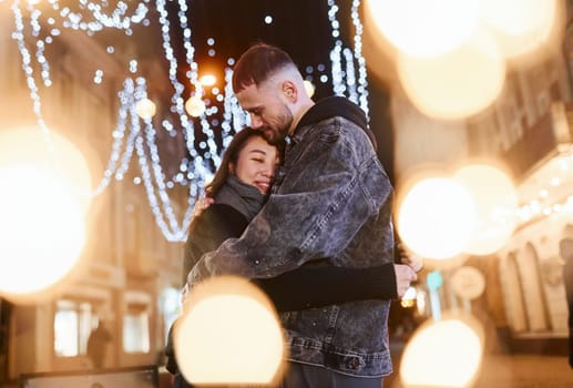 Artificial lighting by garlands. Happy multiracial couple together outdoors in the city celebrating New year.