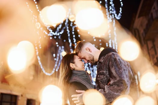 Artificial lighting by garlands. Happy multiracial couple together outdoors in the city celebrating New year.