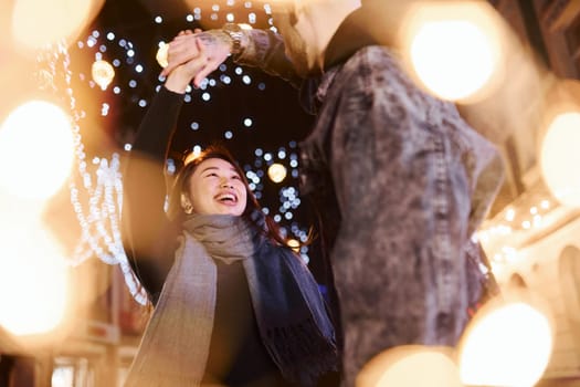 Artificial lighting by garlands. Happy multiracial couple together outdoors in the city celebrating New year.