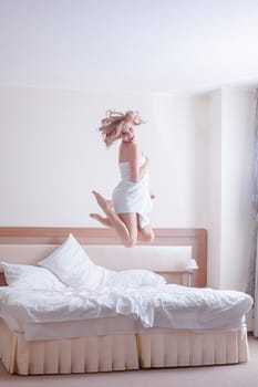 Full length portrait of happy young woman jumping on bed