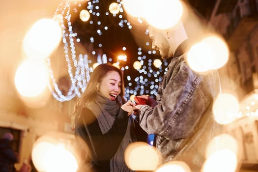 Holds gift box. Happy multiracial couple together outdoors in the city celebrating New year.