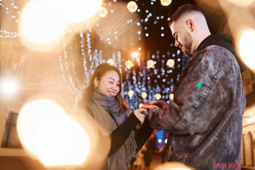 Holds gift box. Happy multiracial couple together outdoors in the city celebrating New year.