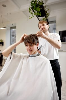 young caucasian man getting haircut by professional male hairstylist at barber shop.