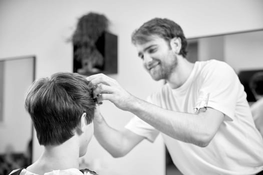 young caucasian man getting haircut by professional male hairstylist at barber shop. black and white