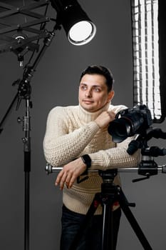 Professional handsome photographer with digital camera on tripod on gray background with lighting equipment