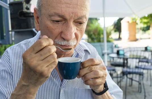 Lifestyle concept. An elderly man drinking espresso coffee at an outdoor cafe in the early hours of the morning before work.
