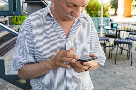 An elderly man holds a mobile phone while waiting for his morning coffee in a cafe.