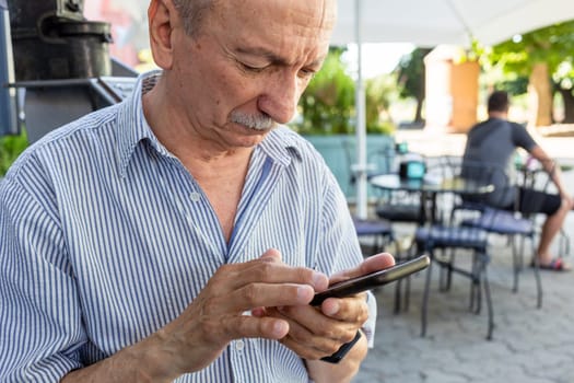 An elderly man holds a mobile phone while waiting for his morning coffee in a cafe.