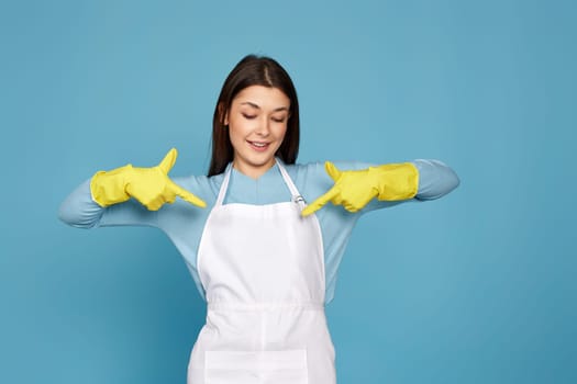 happy caucasian woman in yellow rubber gloves pointing oneself with fingers on blue background. cleaning