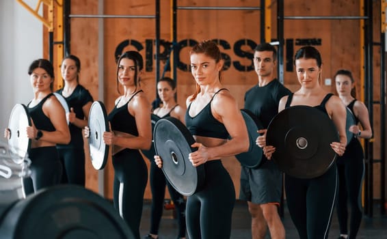 Holding weights. Group of young sportive people have crossfit day indoors in gym.