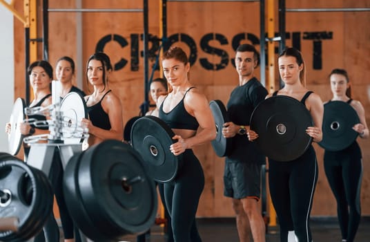 Holding weights. Group of young sportive people have crossfit day indoors in gym.