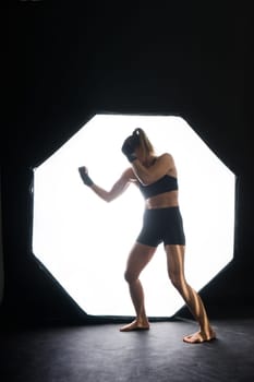 Strong sportswoman in boxing gloves prepared high kick. Isolated on a white, red, yellow background