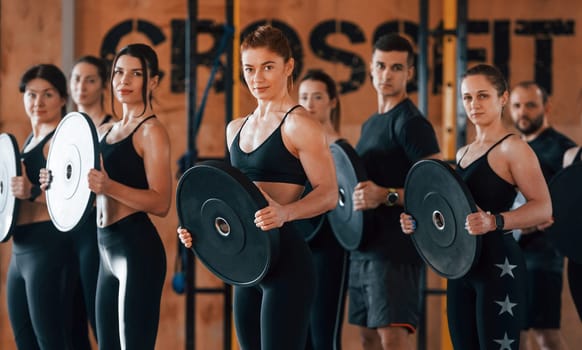 Holding weights. Group of young sportive people have crossfit day indoors in gym.