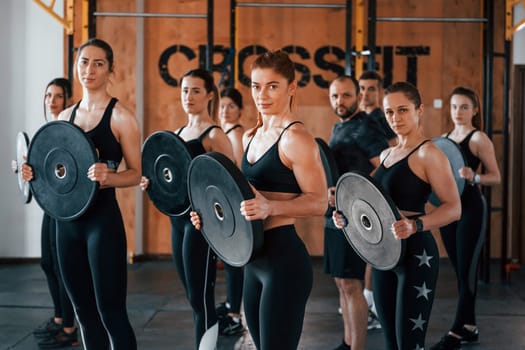 Holding weights. Group of young sportive people have crossfit day indoors in gym.