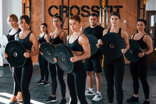 Holding weights. Group of young sportive people have crossfit day indoors in gym.